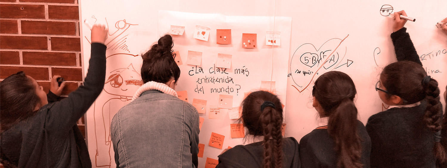 Niñas junto a su profesora dibujando y escribiendo en  el pizarrón. 