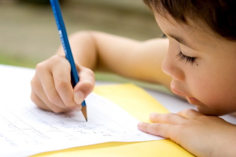 La imagen muestra a un niño escribiendo letras en un cuaderno