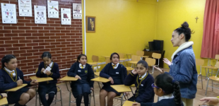 La imagen muestra un círculo de estudiantes con una profesora 