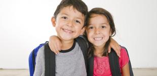 La imagen muestra un niño y una niña abrazados y sonrientes mientras posan para la fotografía