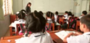 La imagen muestra una sala de clases con niños, niñas y una profesora