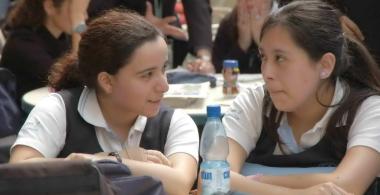 dos mujeres estudiantes conversan en una sala de clases