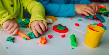 La imagen muestra los brazos de dos niños que están realizando figuras con masas