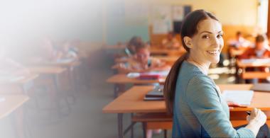 Fotografía de docente en sala de clases, sonriendo a la cámara.
